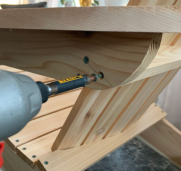 A woodworker driving screws into the arms of a DIY Adirondack chair project built with Bob Vilas downloadable project plans.