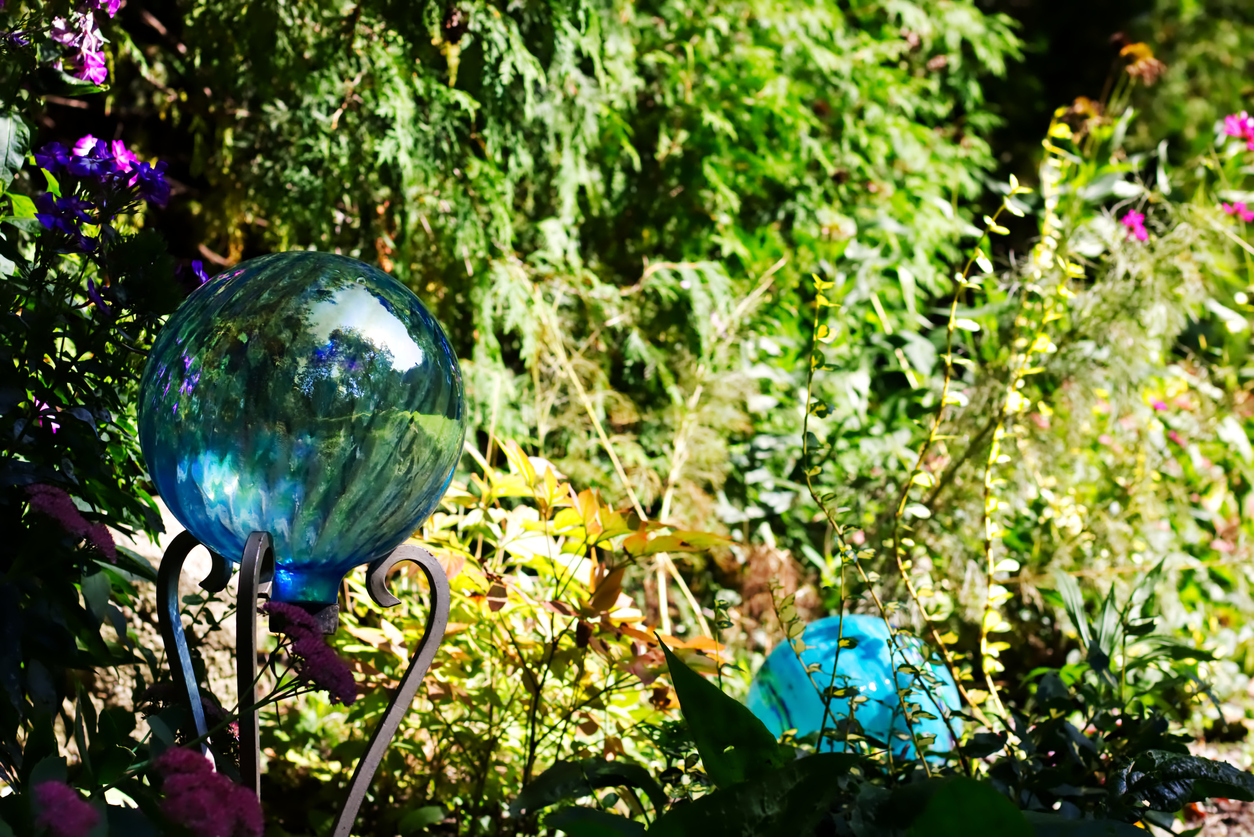 A-blue-glass-gazing-ball-sits-on-a-stand-in-a-lush-green-garden-near-another-blue-sphere.