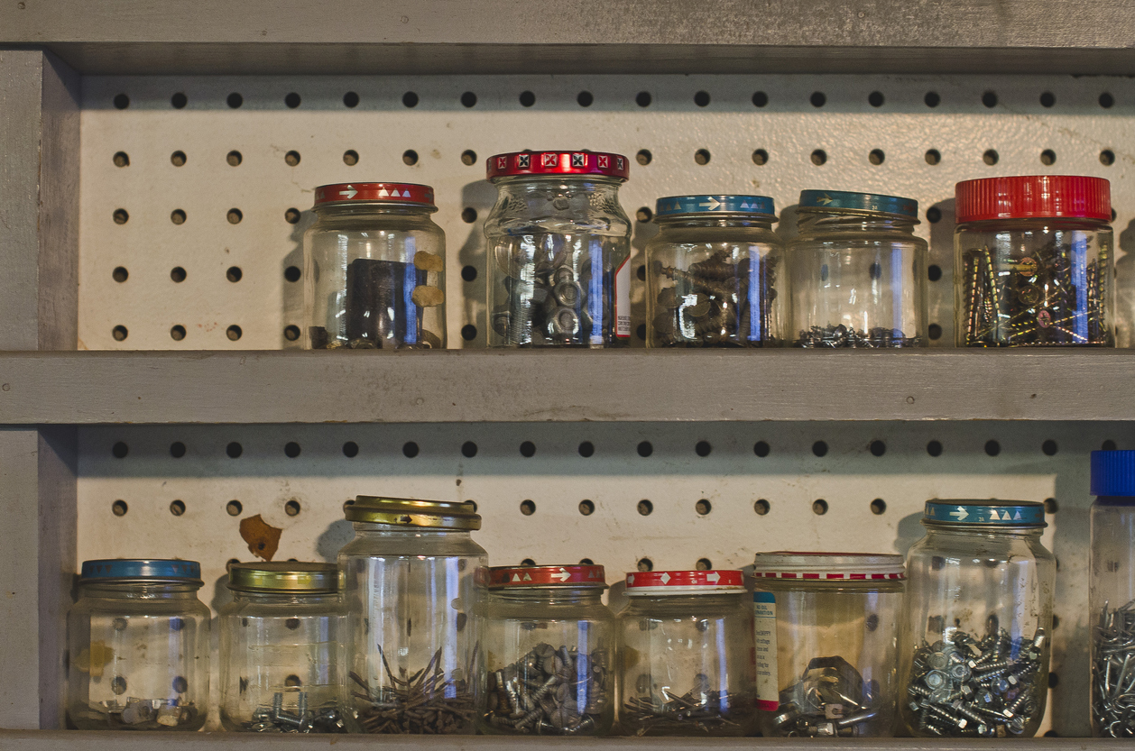 A row of wooden shelves in a old dusty work shop full of glass jars and screws in the old shop keeping everything stored.