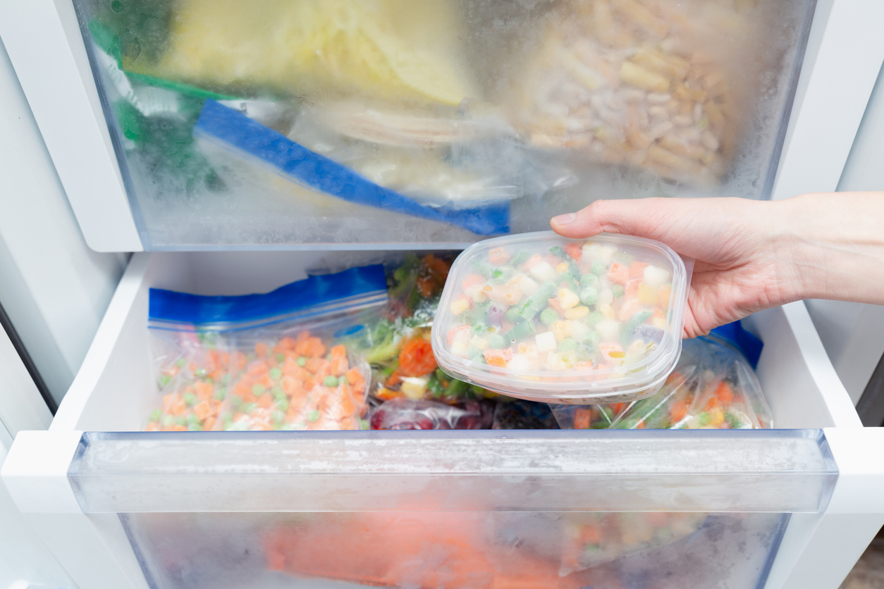 Frozen vegetables in a plastic bag being placed inside a freezer full of frozen food packages.