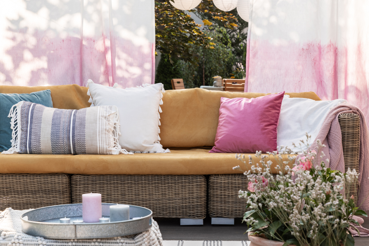 Colorful pillows on rattan sofa on the terrace with flowers, painted drapes and candles.