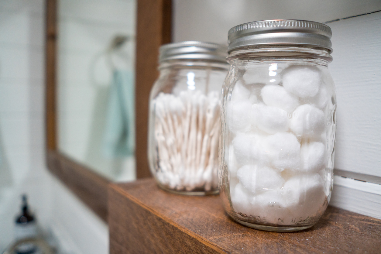 Cotton balls and cotton swabs in mason jars on farmhouse bathroom shelf.