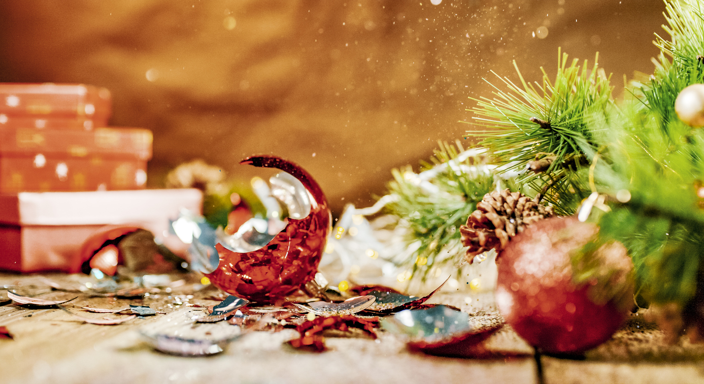 A broken christmas ornament on a wood surface with pine needles and other Christmas decorations.