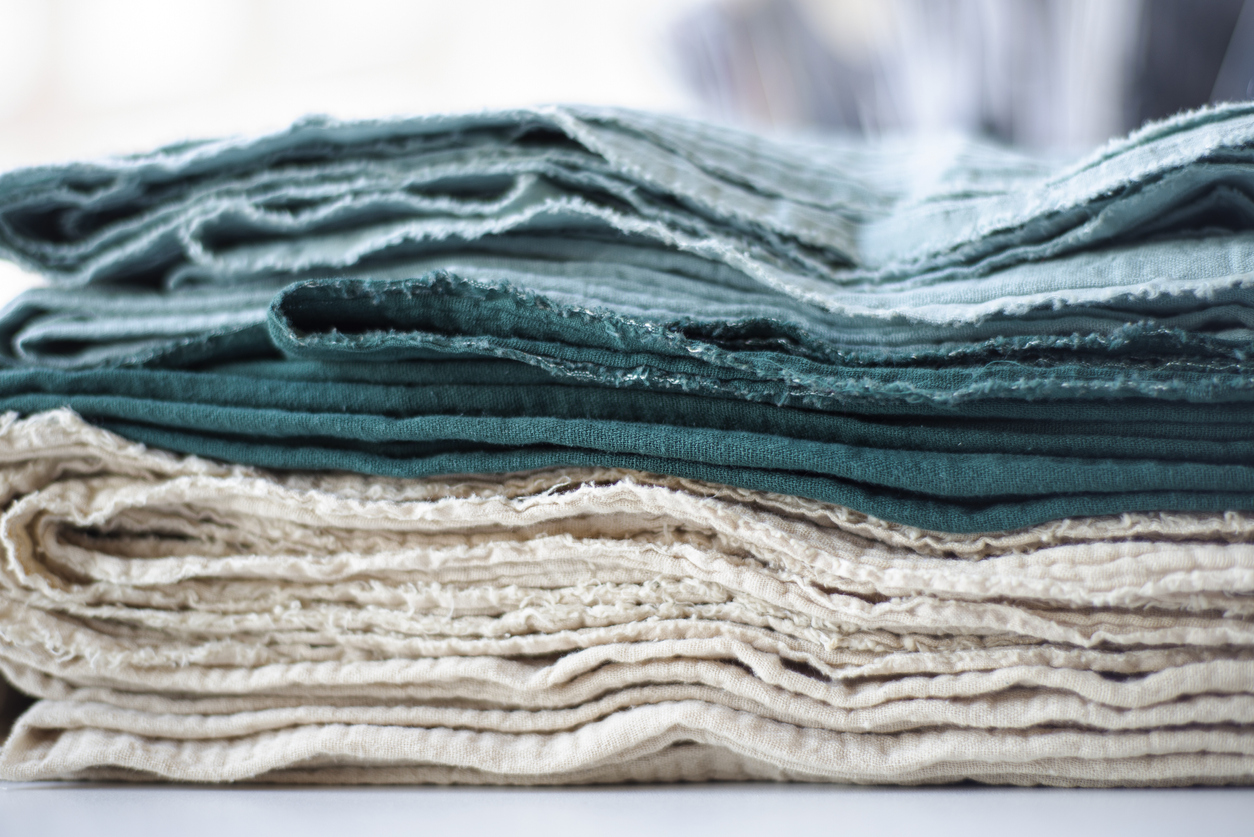 Cotton textiles in shades of green and beige in a stack with frayed edges.