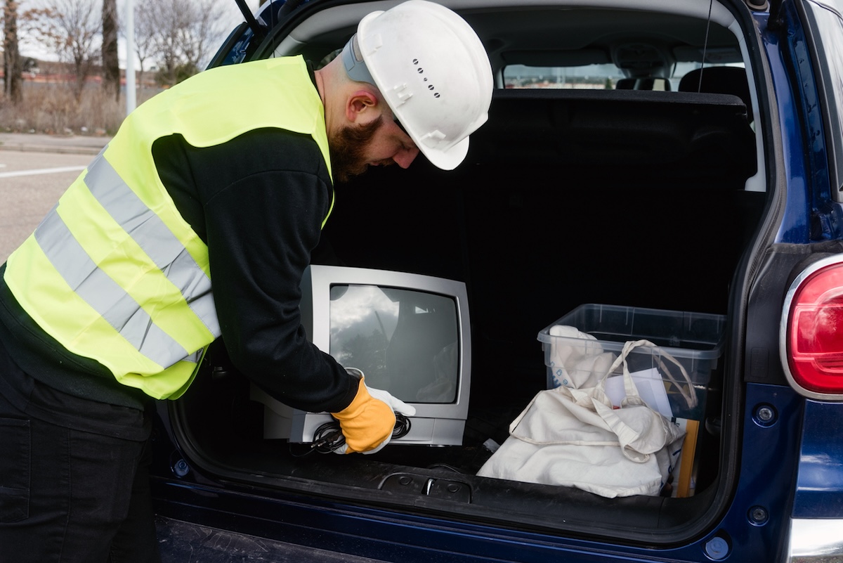 A sanitation worker unloading an old TV out of a trunk for e-waste recycling.