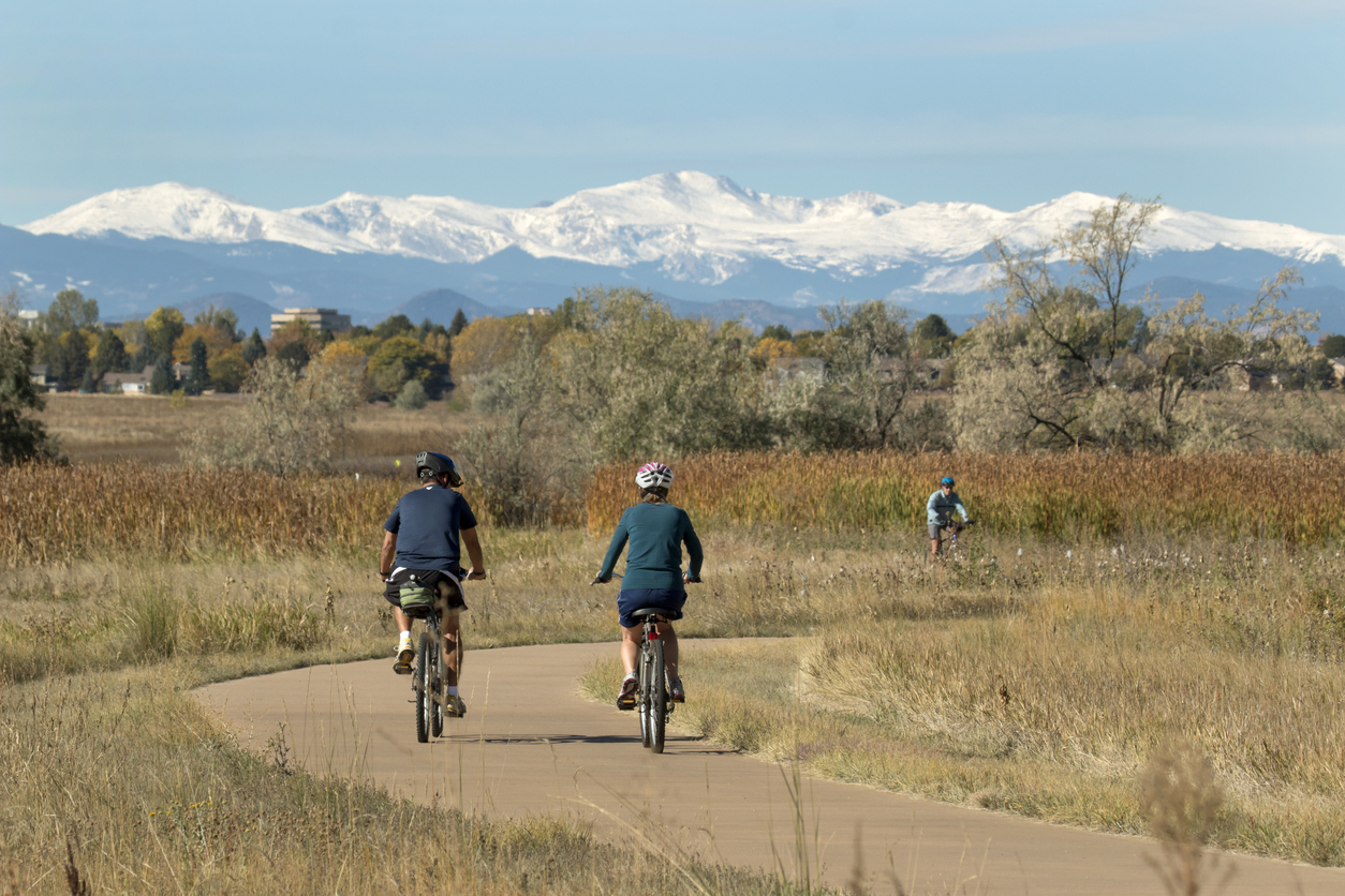 Riding the paved path around the lake with a snowy Mount Evans in the background, visitors enjoy riding their bicycles in Colorado's Cheery Creek State Park in Denver.