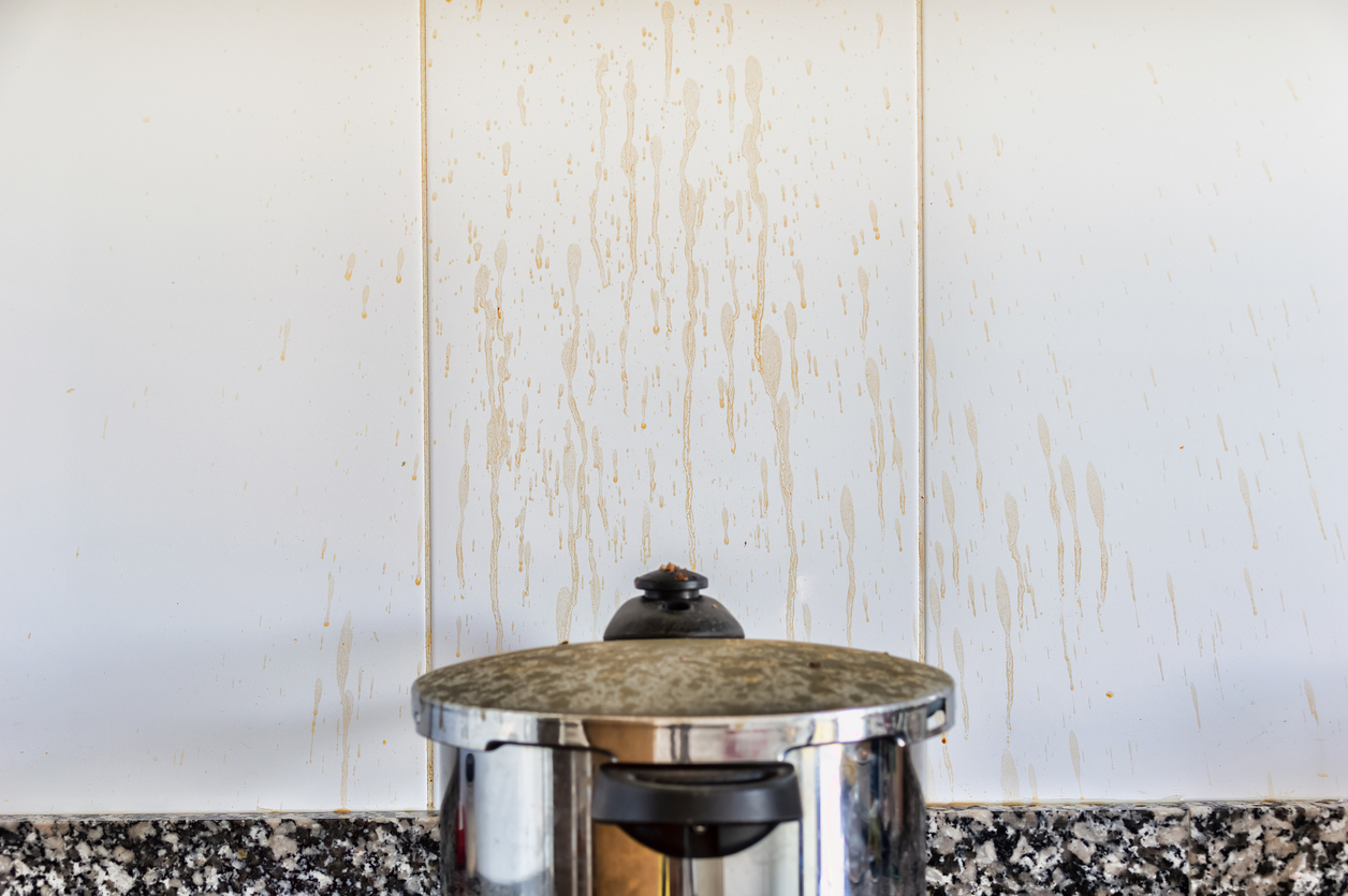 A pot on the stove with in front of a backsplash covered in grease stains from cooking.