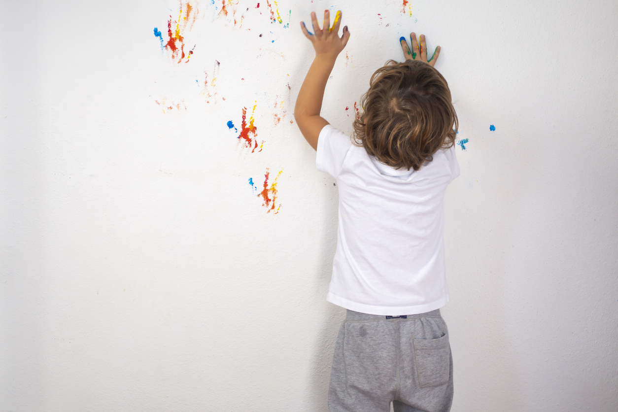 A small boy plays with finger paint by leaving marks on a white wall.