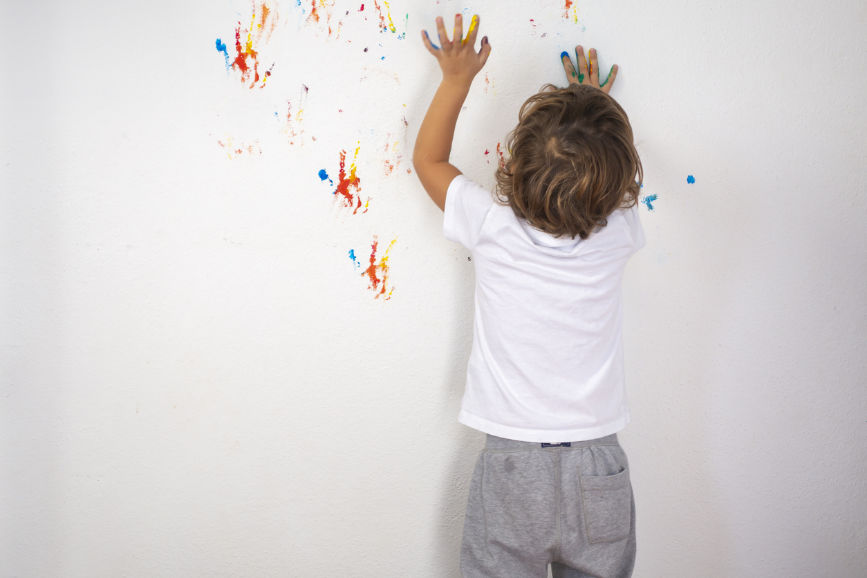 A small boy plays with finger paint by leaving marks on a white wall.