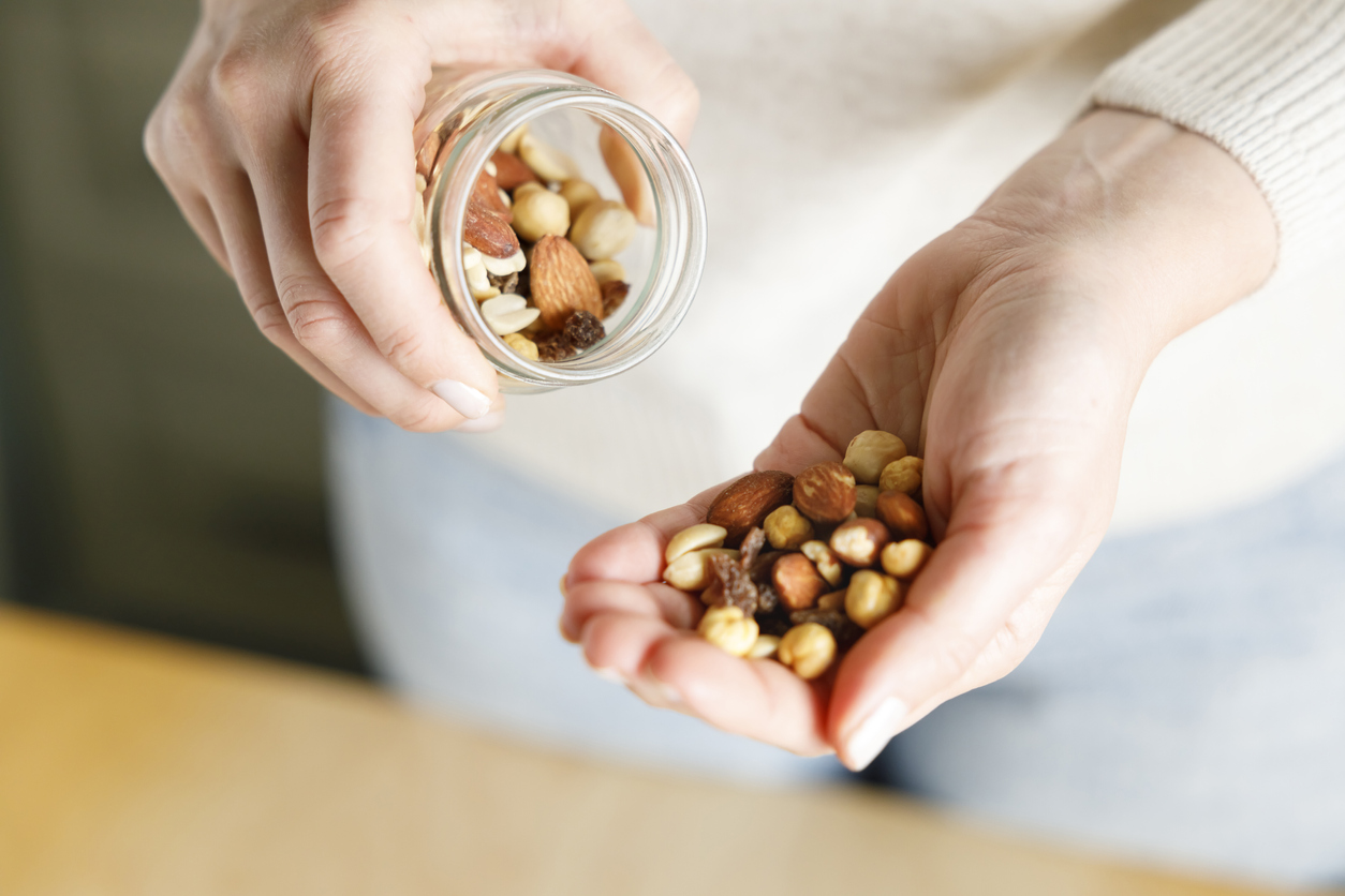 A woman pours a handful of nuts from a jar into her hand.
