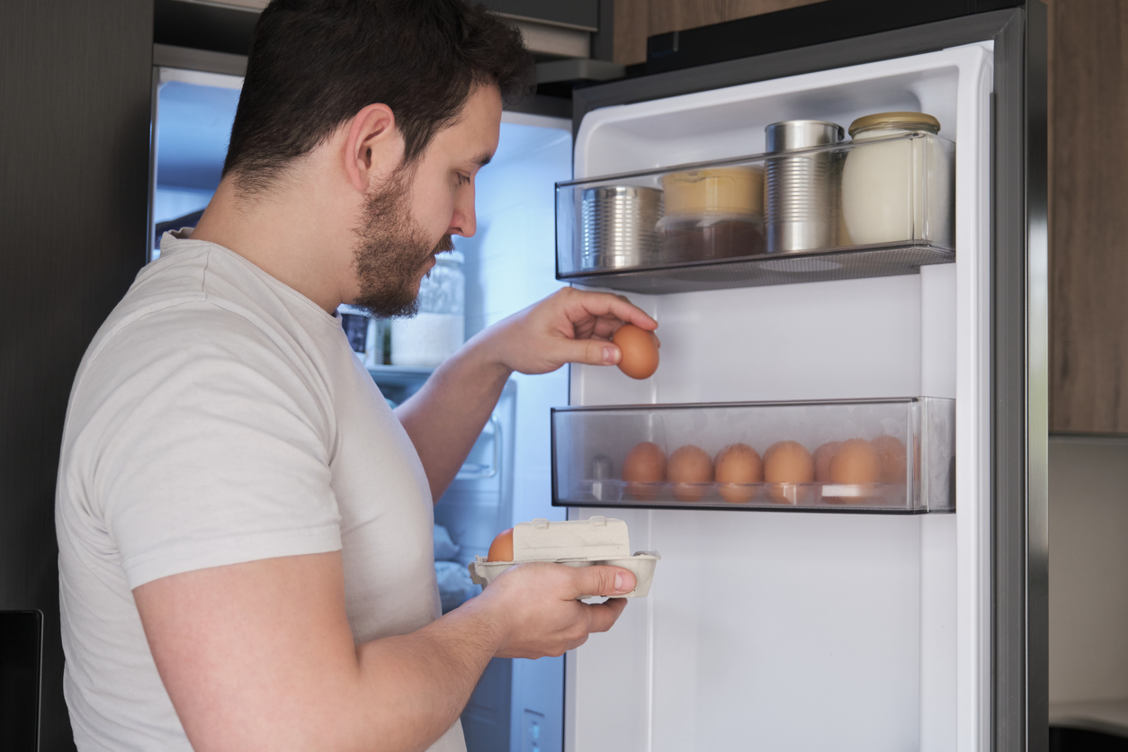 Young latin man placing eggs in the fridge door shelf.