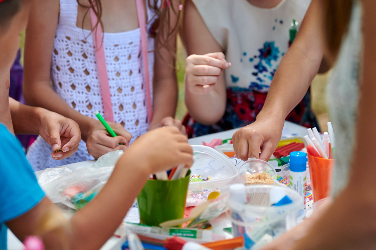 A group of children gathered around a craft table with art supplies making doing crafts.