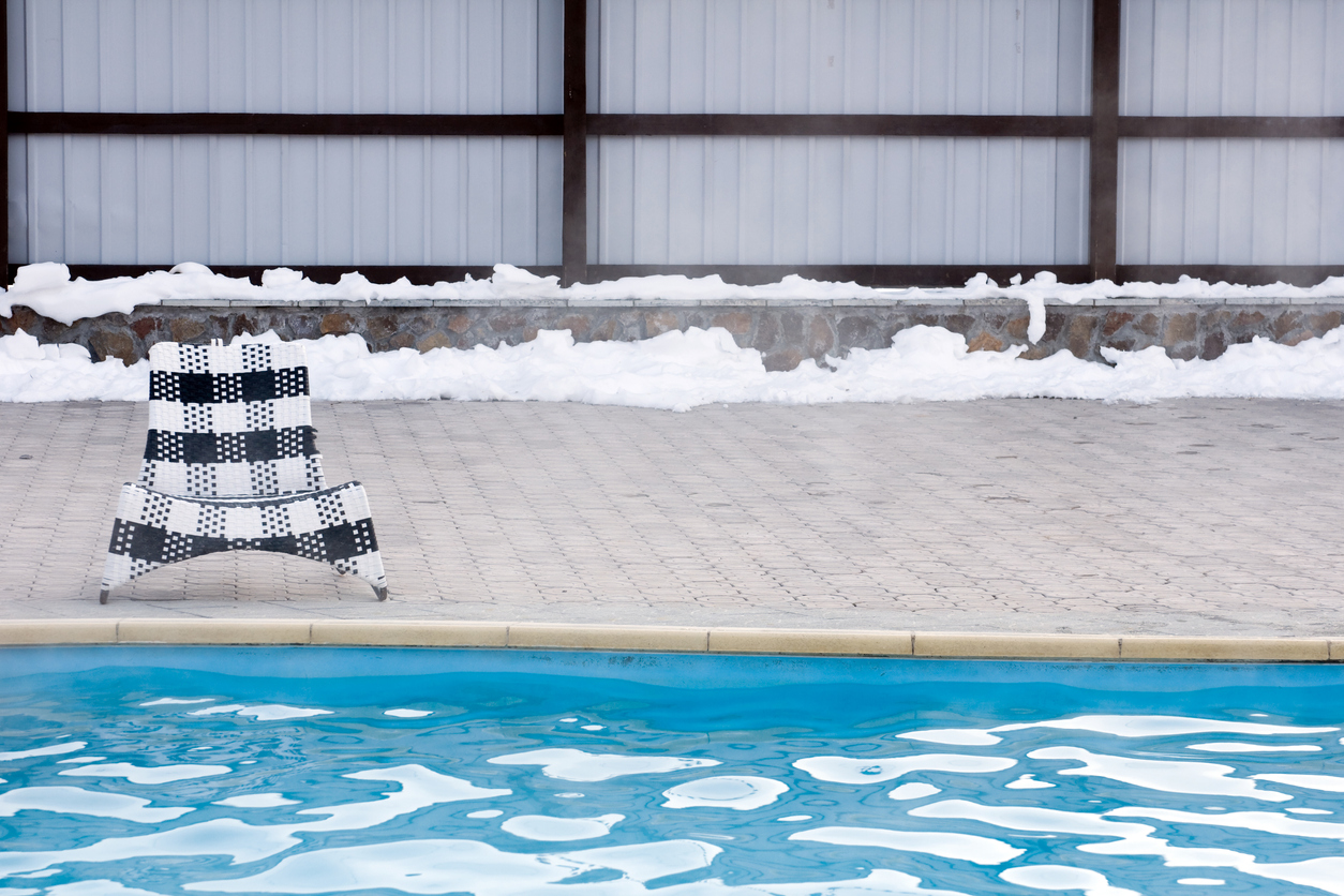 A-black-and-white-checked-chair-sits-on-the-edge-of-a-swimming-pool-with-floating-ice.
