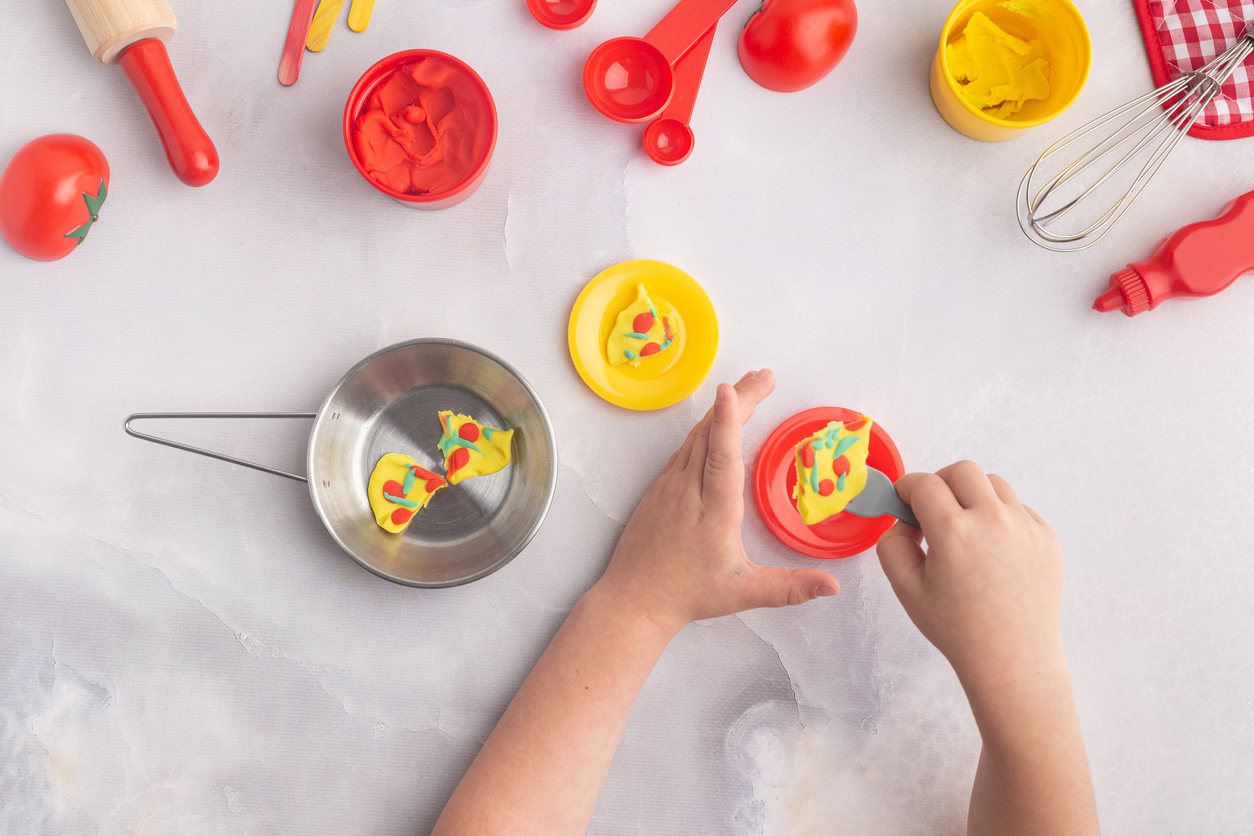 Overhead view of a boys hands as he makes pretend food with play dough and toy baking things.