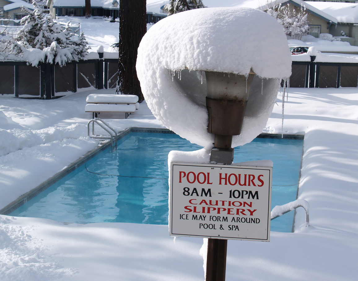 Snow-covers-the-ground-around-a-swimming-pool-and-a-sign-with-pool-hours-is-topped-with-snow.