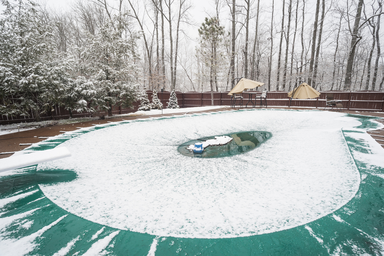 Snow-is-melting-in-the-center-of-a-swimming-pool-cover-surrounded-by-winter-trees