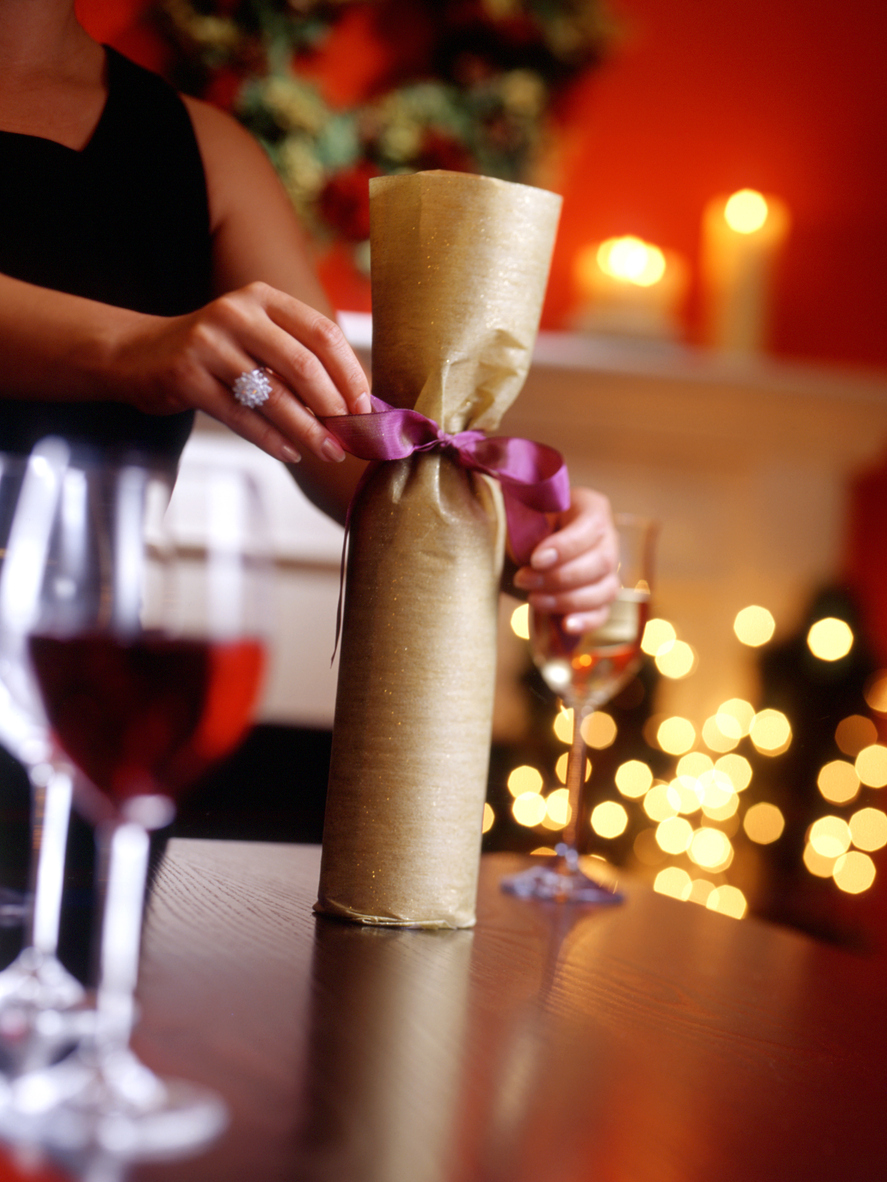 Gift wrapping a wine bottle with ribbon.