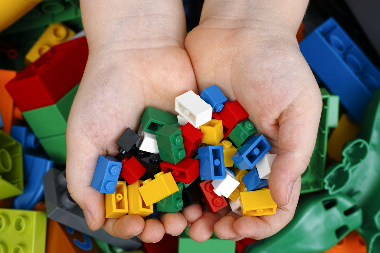 overhead close shot of a child's hands holding a bunch of small lego pieces with a pile of legos underneath.
