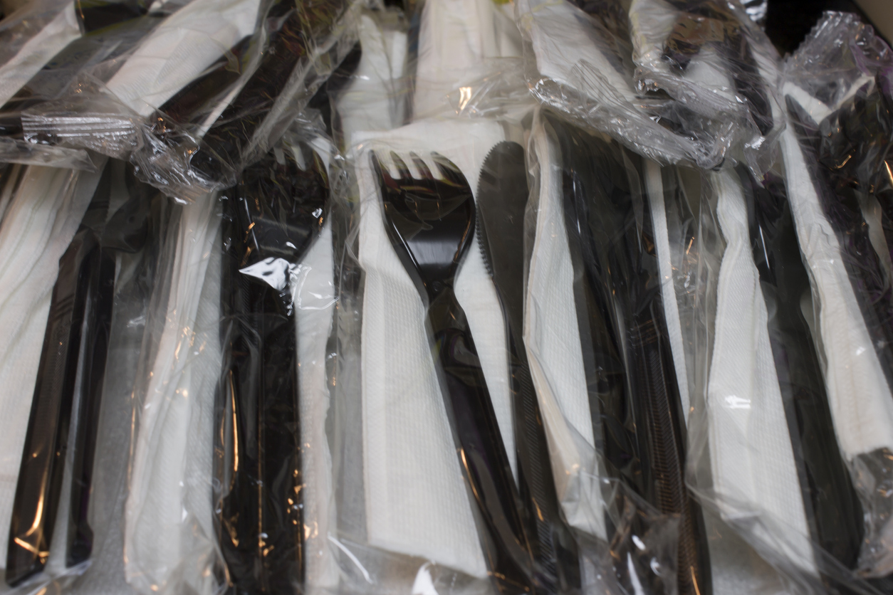 A pile of plastic disposable forks and knives with napkins wrapped in plastic.