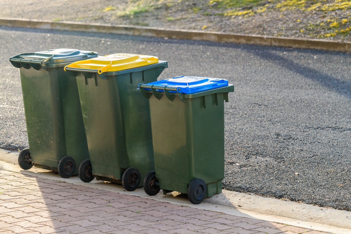 Three waste and recycling bins at the curb in front of a house.