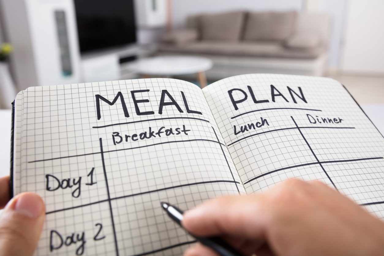 Close-up Of A Human Hand Filling Meal Plan In Checkered Pattern Notebook