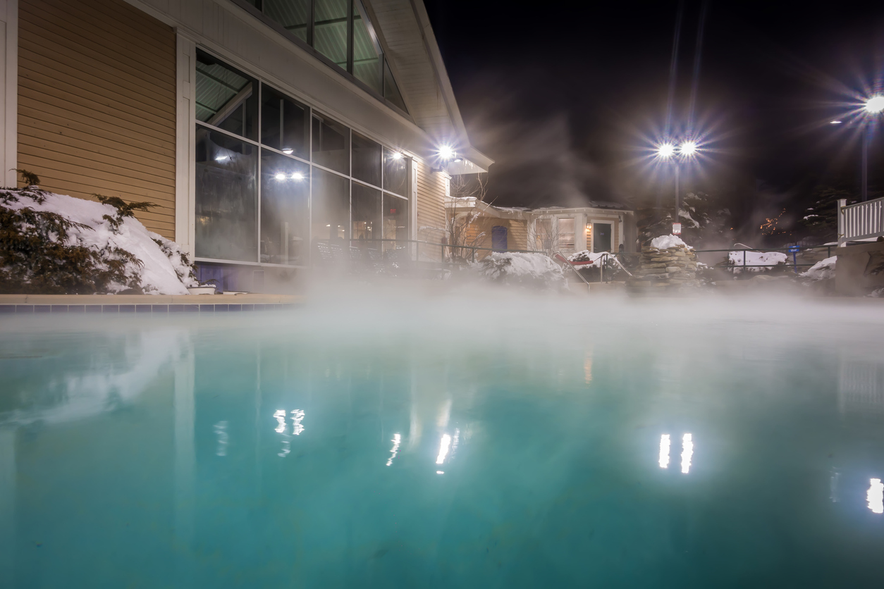 Steam-rises-off-the-top-of-a-swimming-pool-at-night-in-a-snowy-backyard.