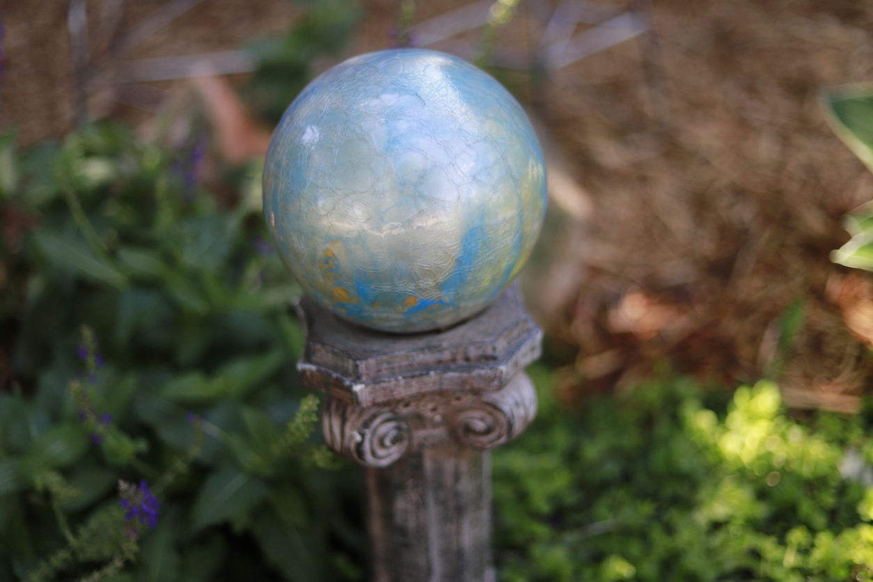 A-silver-metallic-garden-gazing-ball-sits-on-a-pillar-stand-in-a-garden.