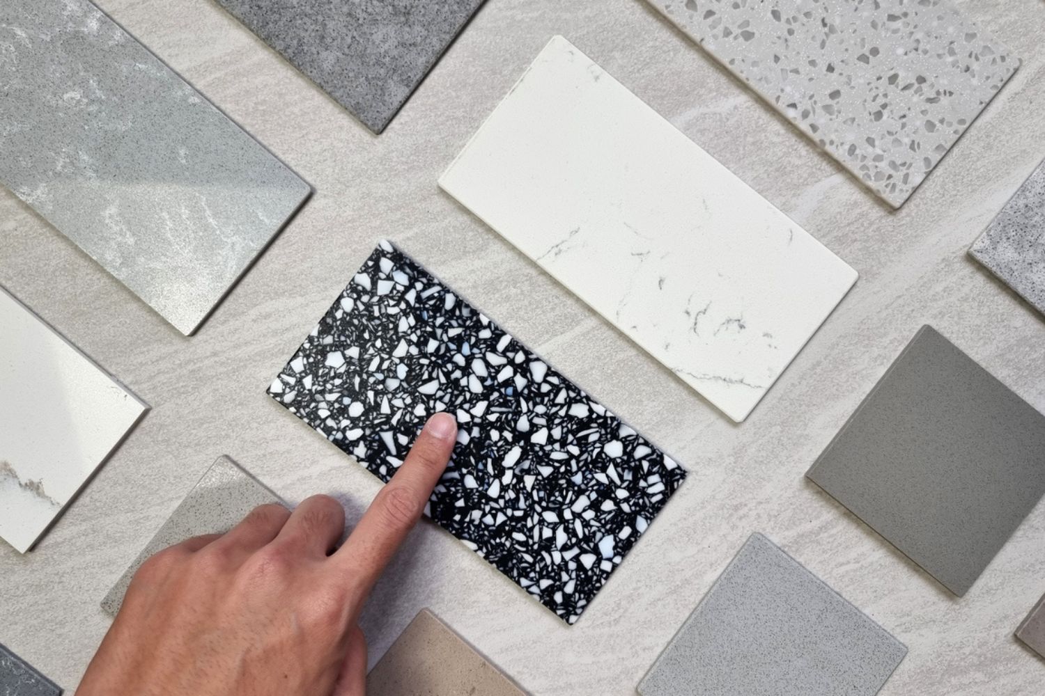 A hand points at a dark terrazzo tile sample.