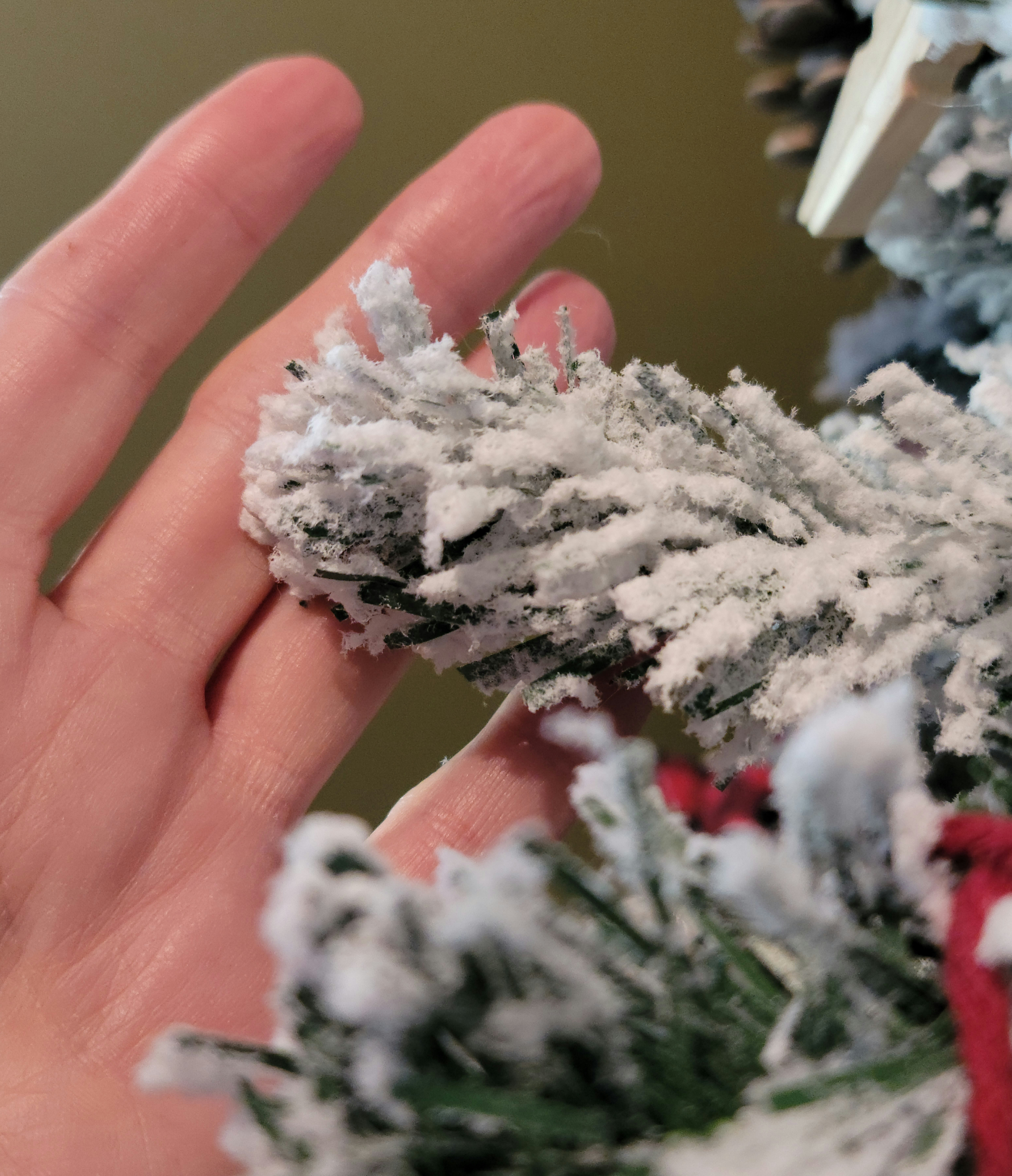 Person's hand lifting the flocked limb of one of the Best artificial Christmas trees.