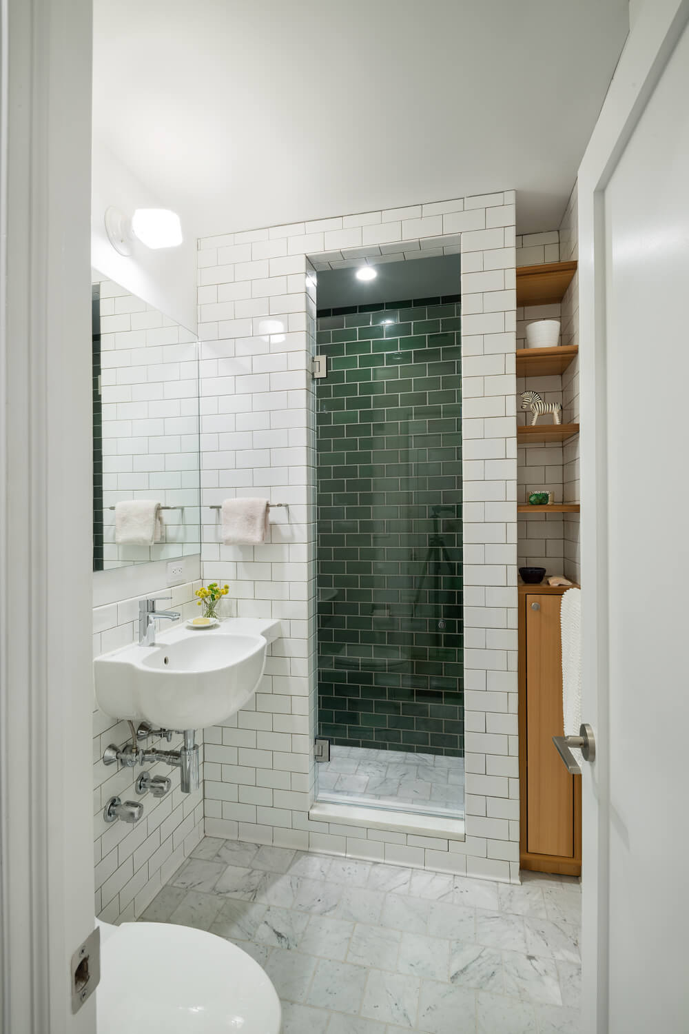 A white bathroom with a walk-in shower with green wall tiles.