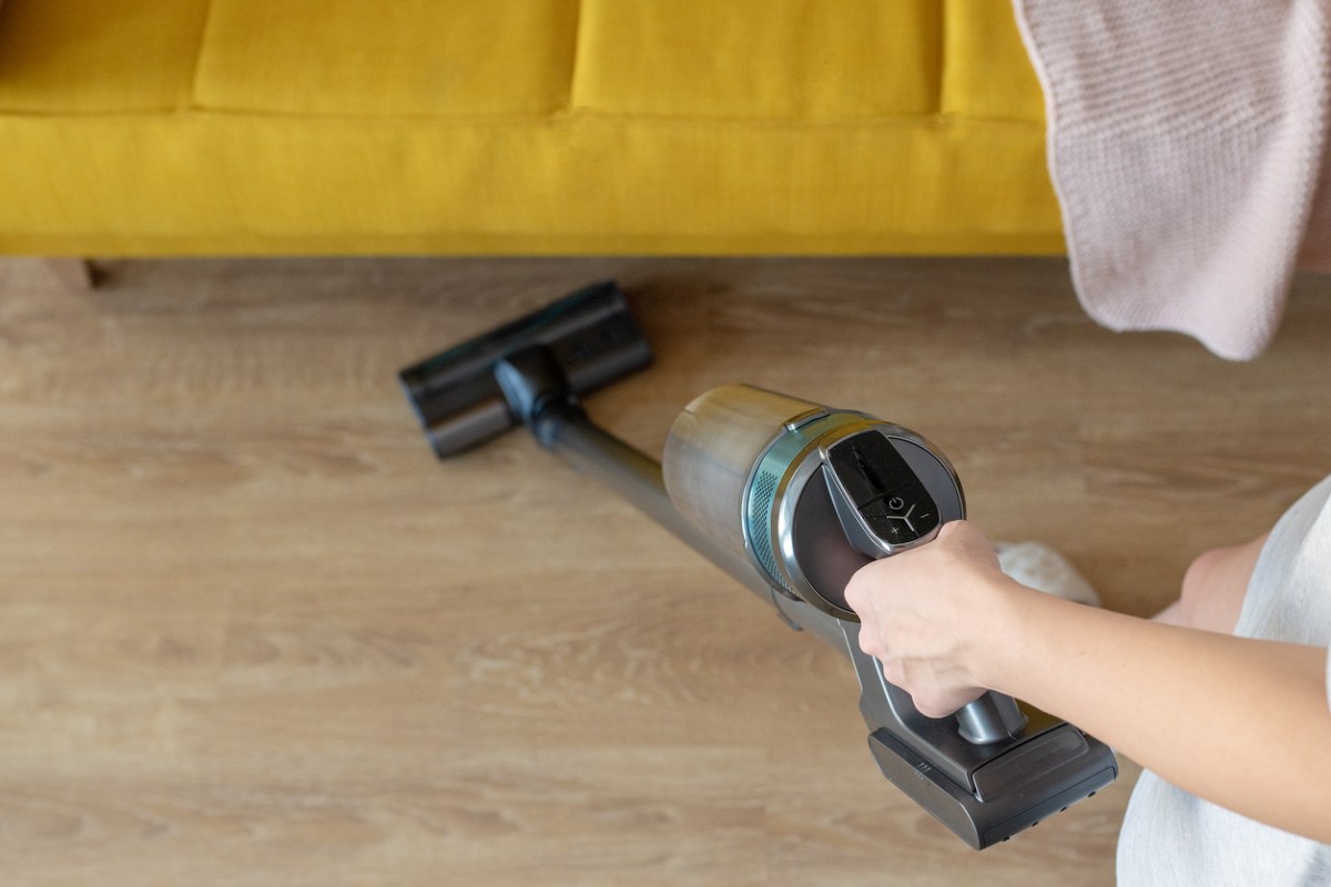 Best A person using the best cheap vacuum to vacuum a laminate floor under a yellow couch. Vacuum