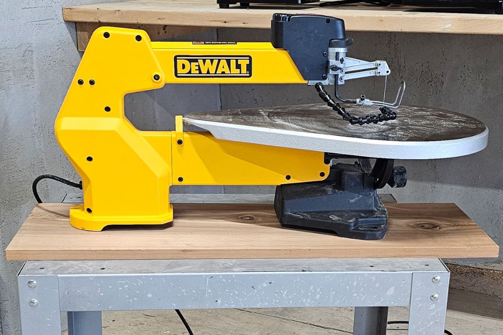 The DeWalt scroll saw on a small work table with a dusty work surface after testing.