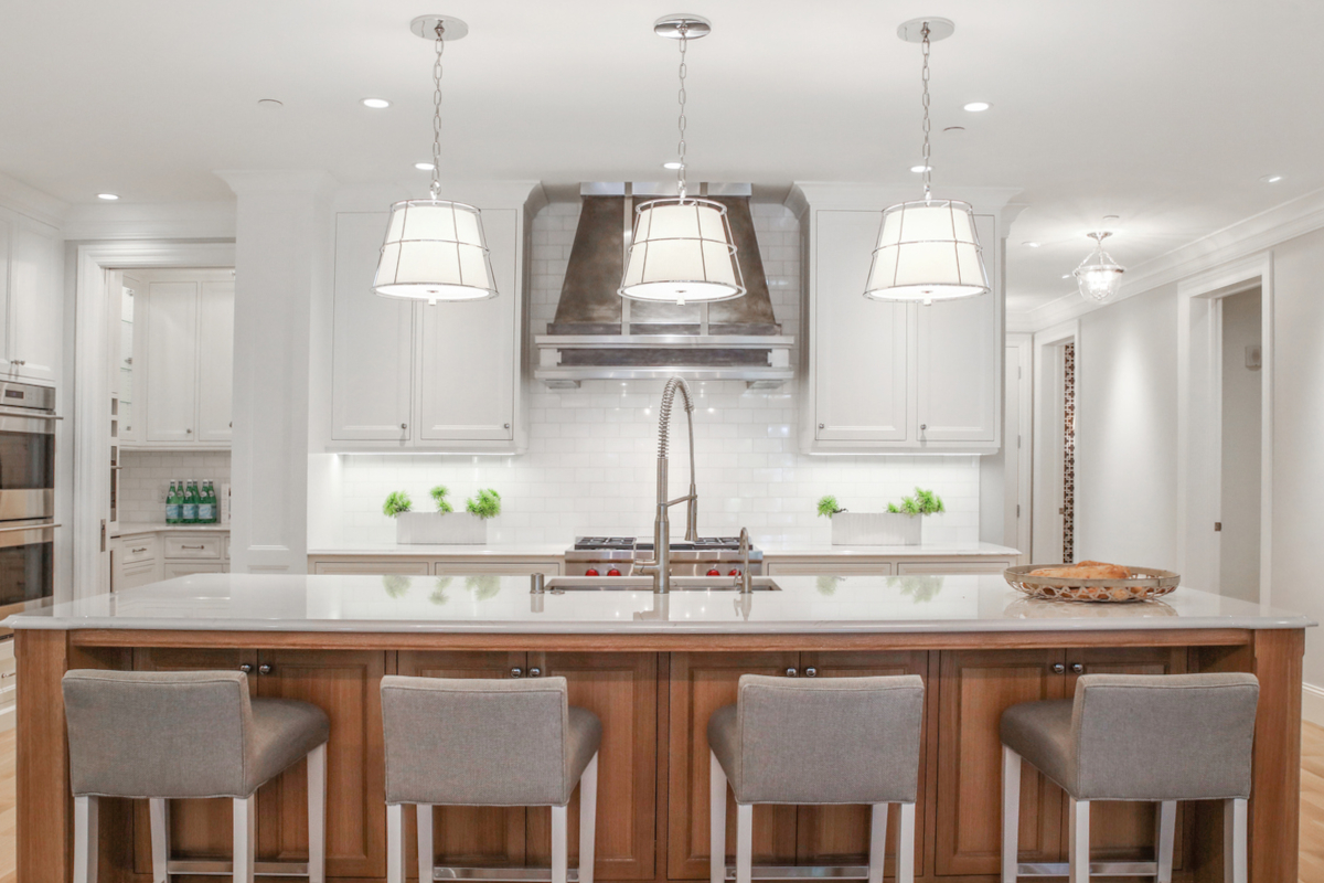 A bright kitchen lit by daylight bulbs in hanging lights and recessed lights.