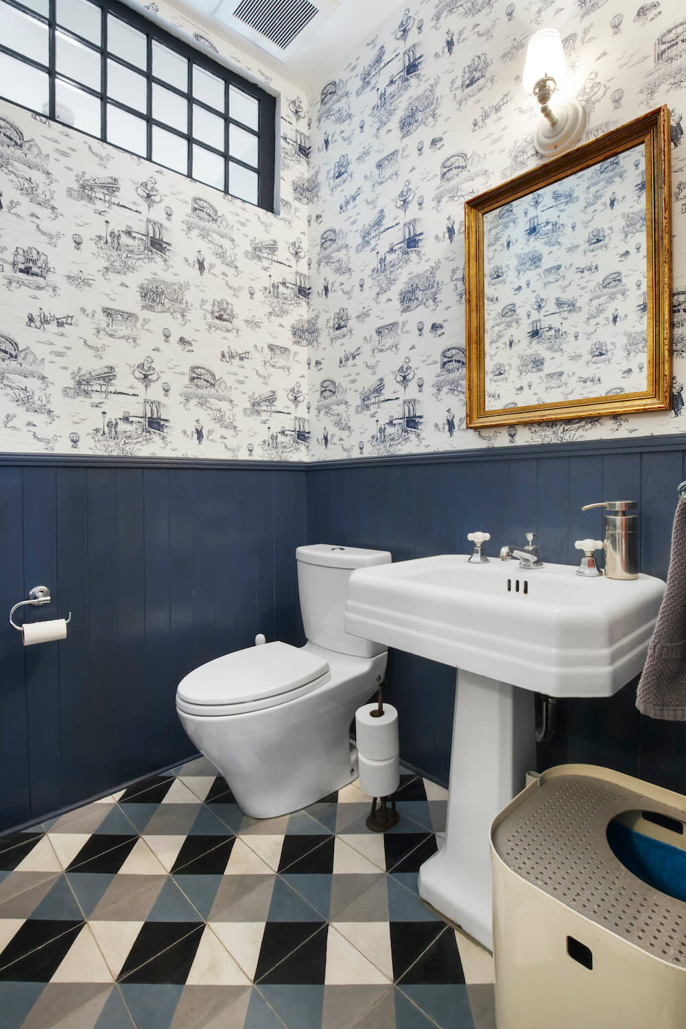 A small bathroom with blue wood wall paneling, white-and-blue patterned wallpaper, and plaid blue-and-white floor tile.