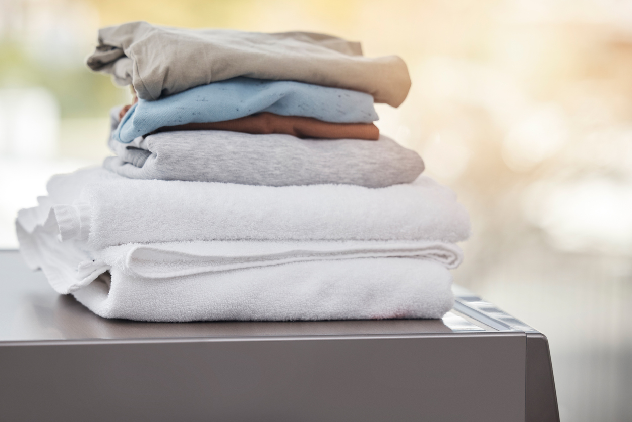 A stack of folded white towels and neutral T-shirts sitting on top of a washing machine.