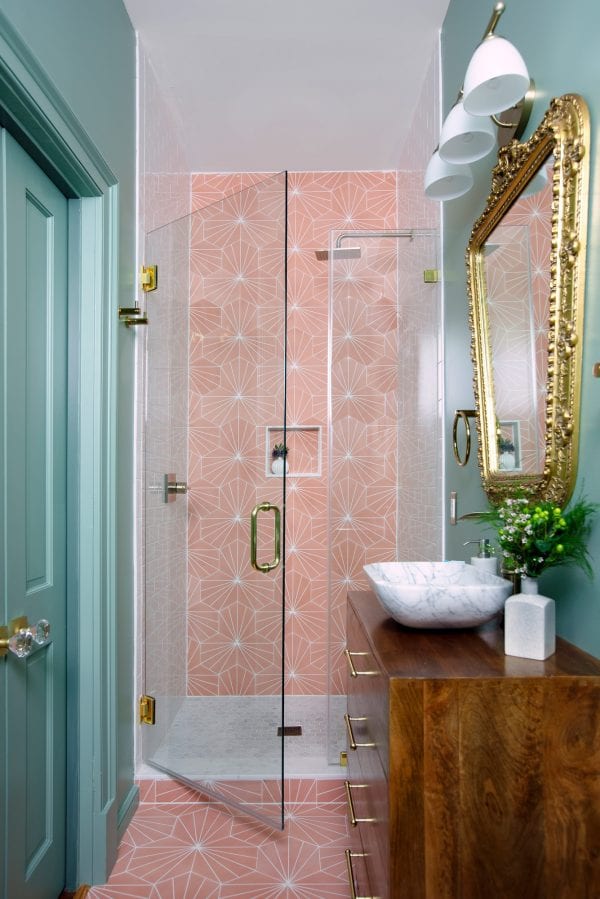 A narrow bathroom with light teal walls and pink shower and floor tile.
