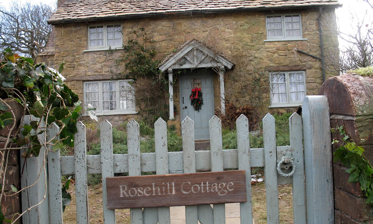 Rosehill Cottage sits behind a white picket fence with a sign bearing its name.
