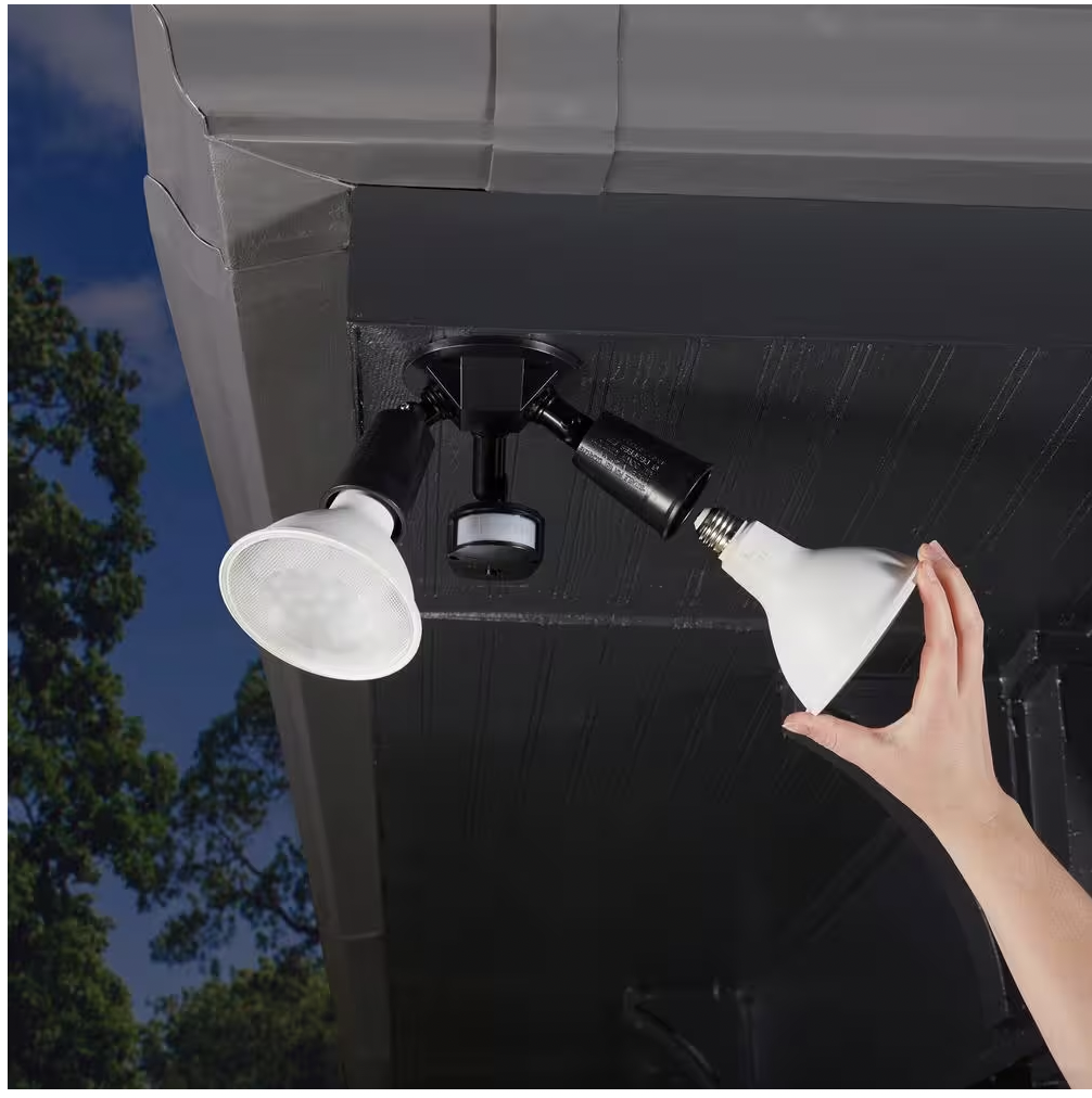 A hand reaches up and installs an LED light bulb under the overhang of a roof.