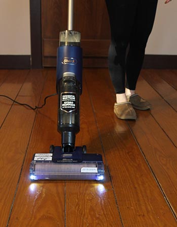 A person using the Shark HydroVac with LED lights to clean hardwood floors.