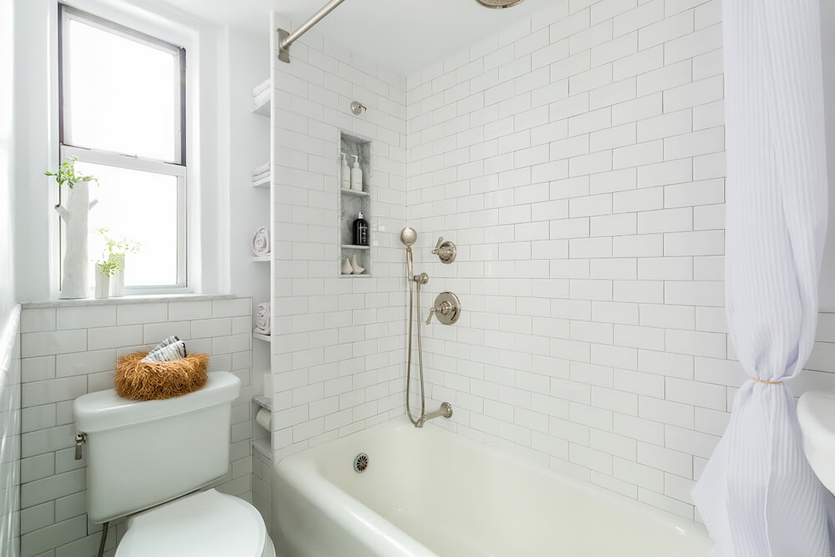 A cramped bathroom with a bathtub-shower combo, toilet, and very narrow floor-to-ceiling shelving.