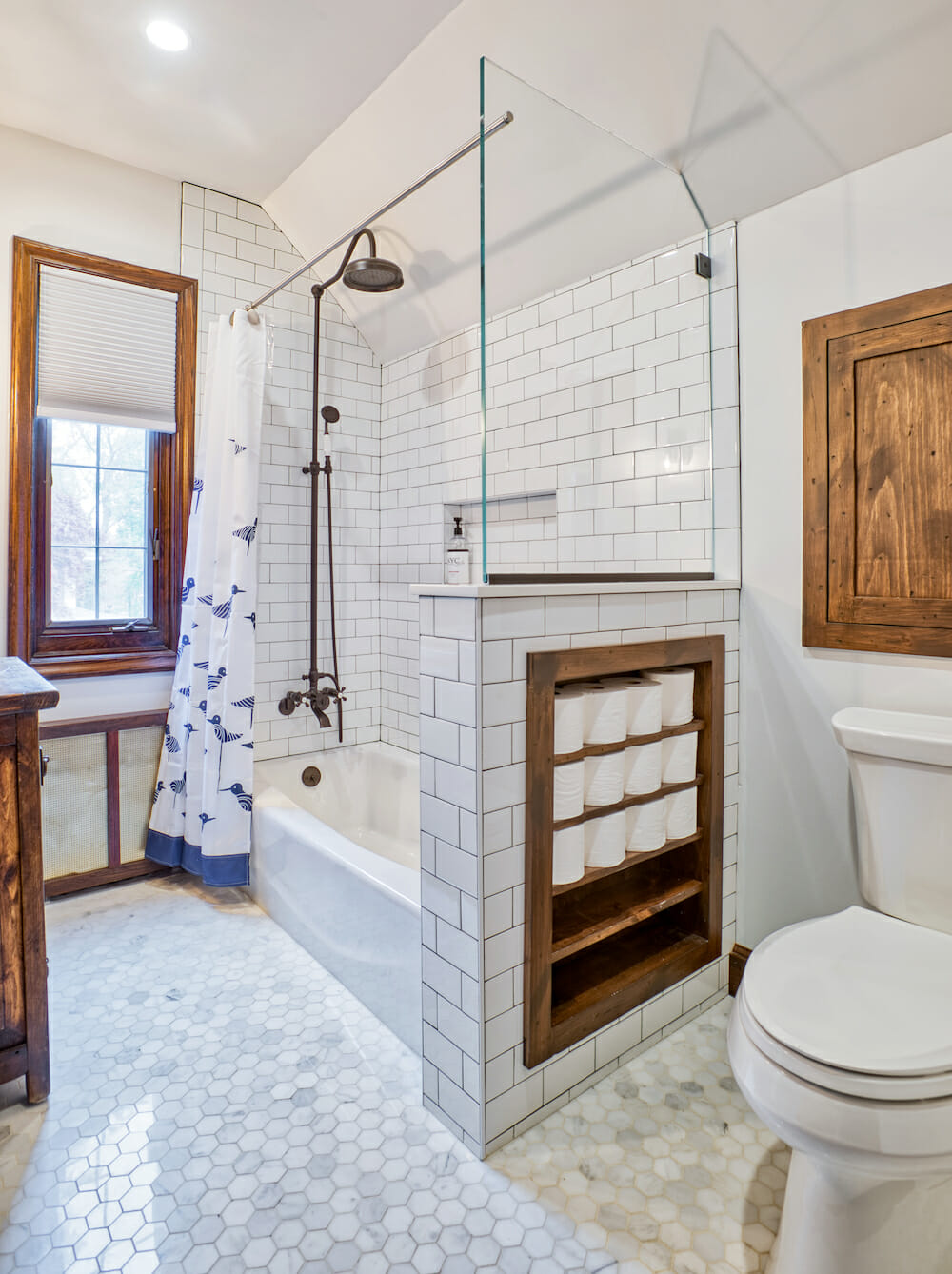 A white bathroom with built-in wood shelves full of toilet paper rolls.