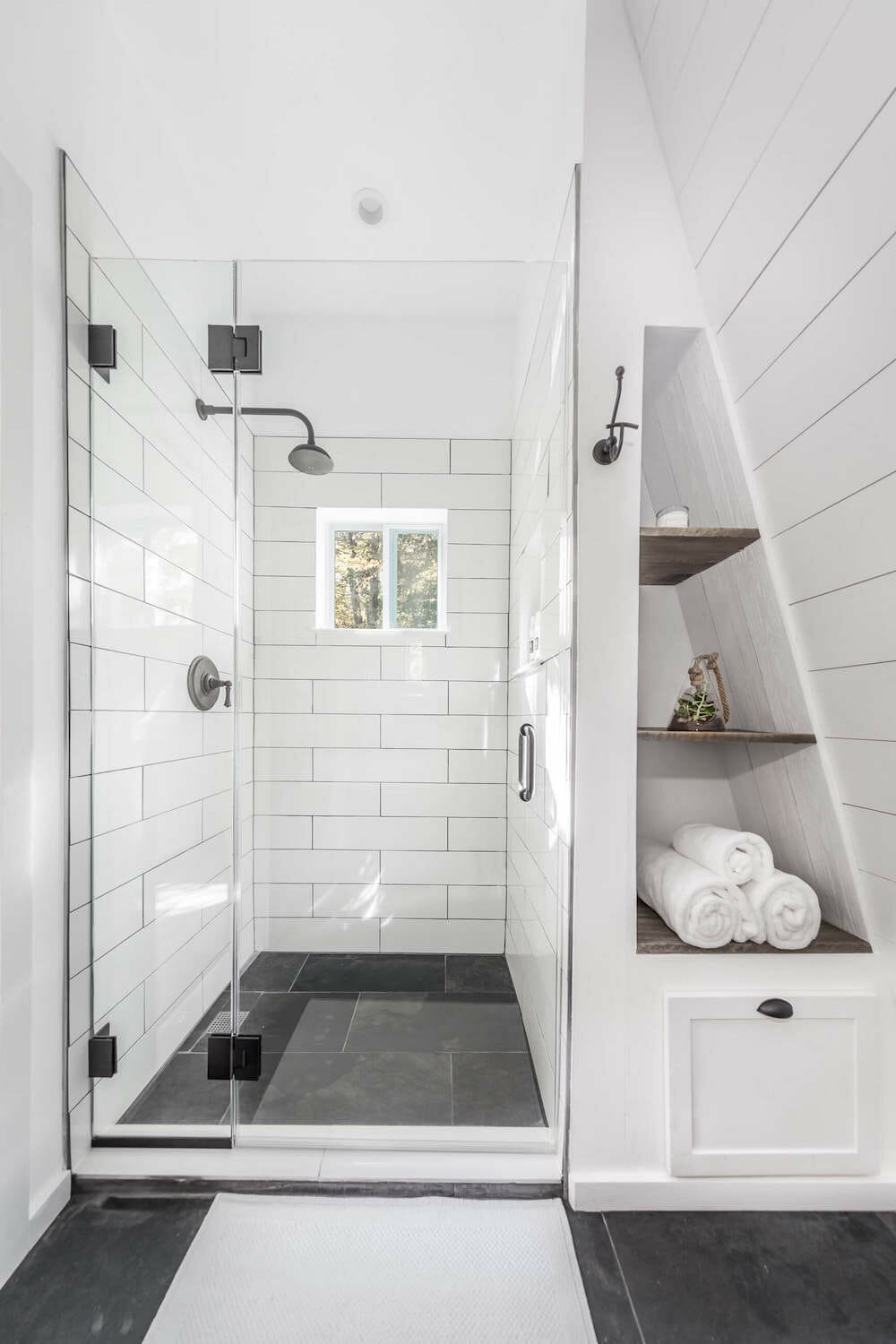 Half of a small bathroom converted from a closet with modern farmhouse decor and shelving built into a sloped wall.