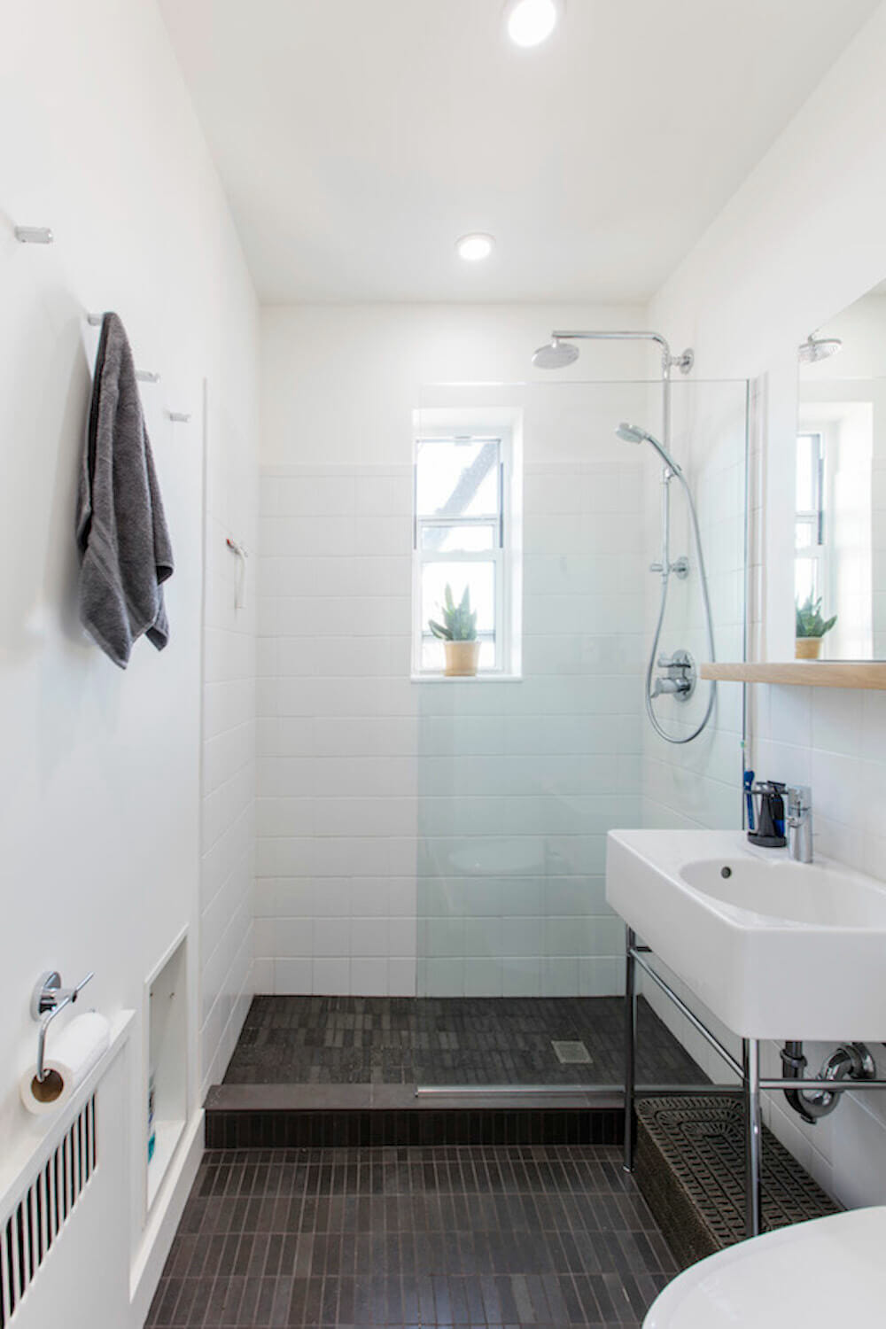 A narrow wet room-style bathroom with white tile walls and dark slate flooring.