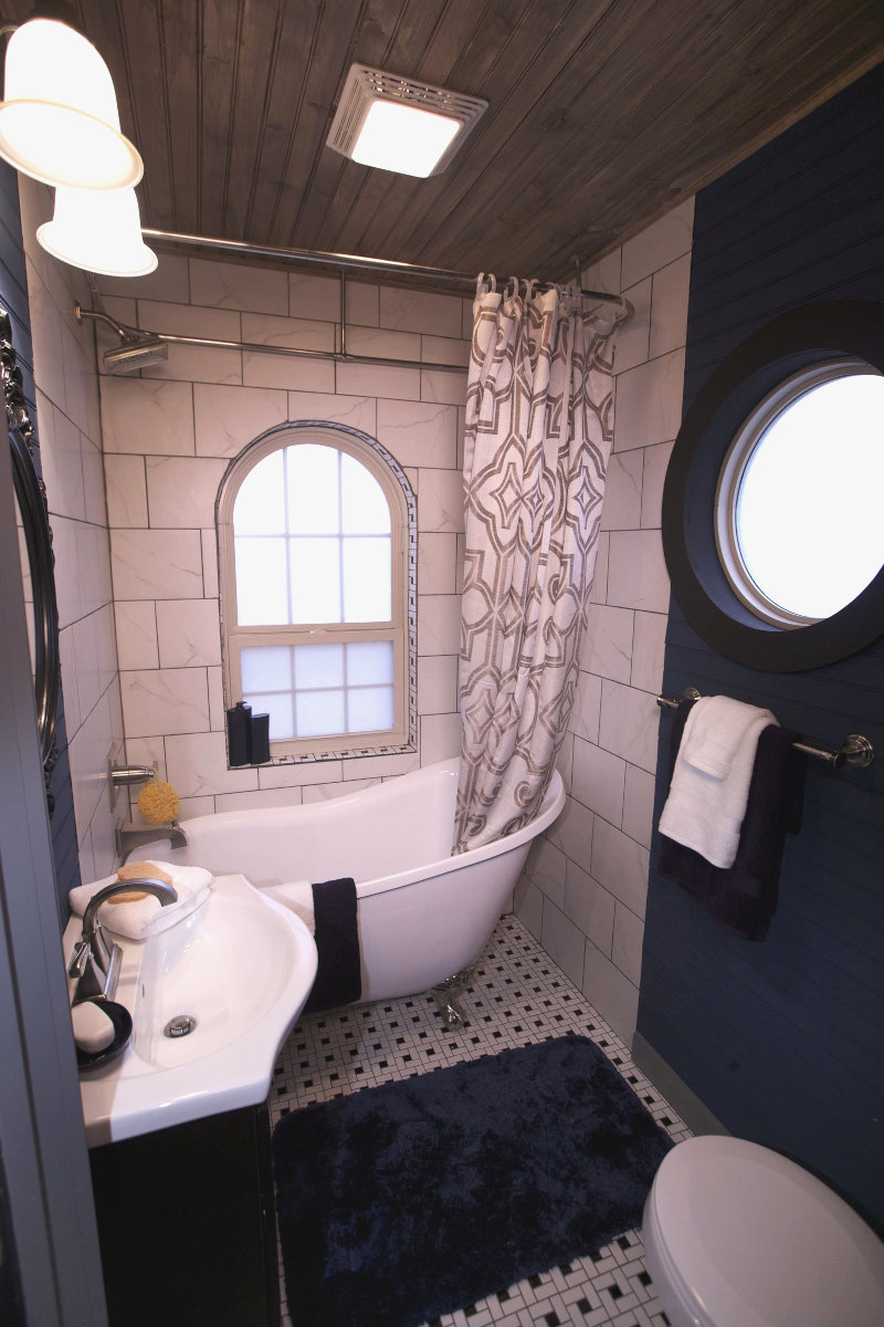 A small bathroom with a circular and arched window on the wall surrounding a a clawfoot bathtub.