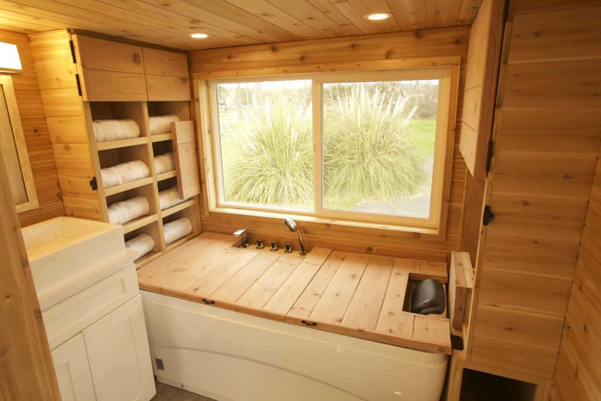 The bathroom in a tiny house with sauna-style wood paneling and bathtub cover-bench combo.