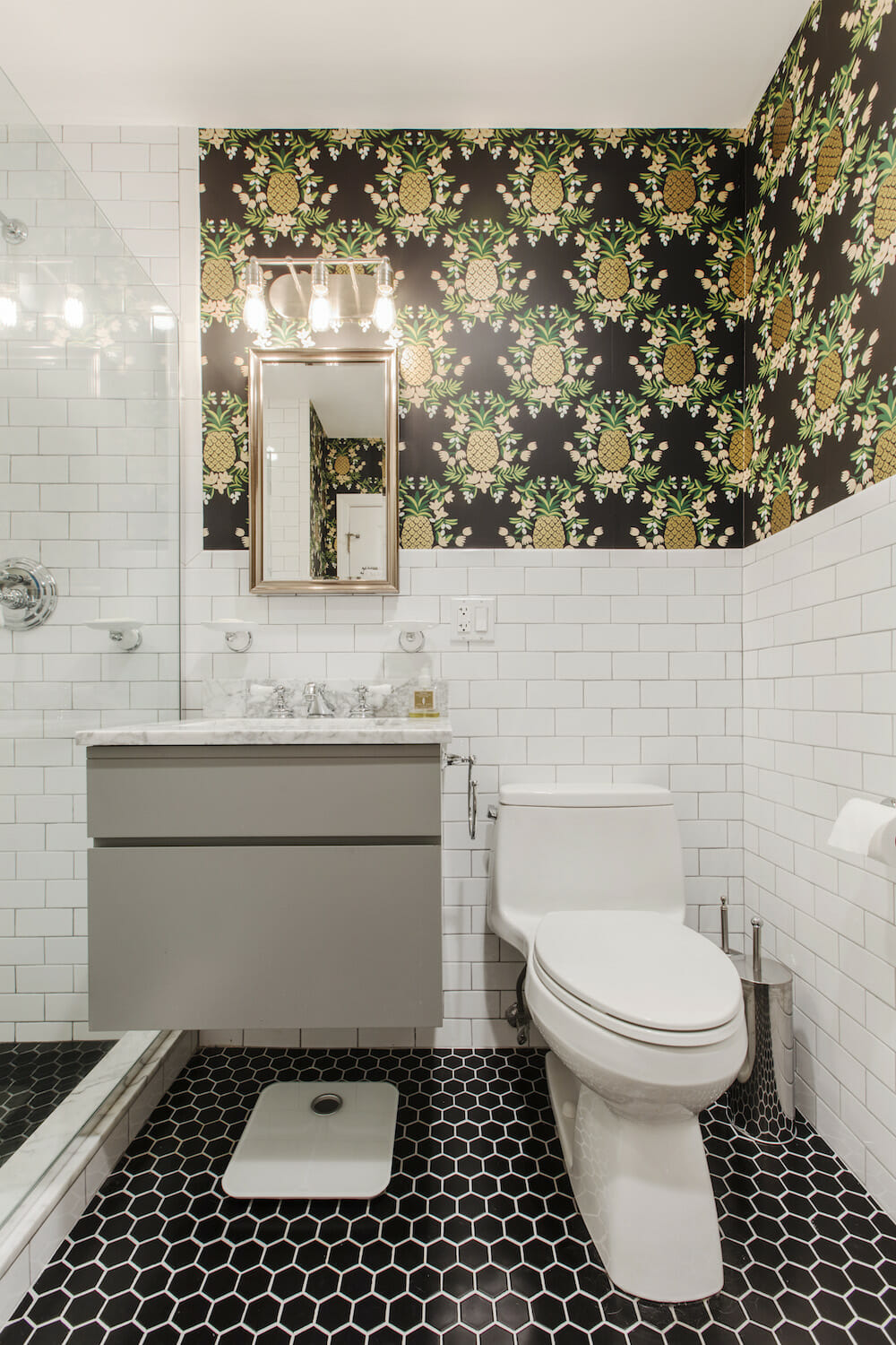The corner of a bathroom with black hex floor tile and gilt pineapple wallpaper.