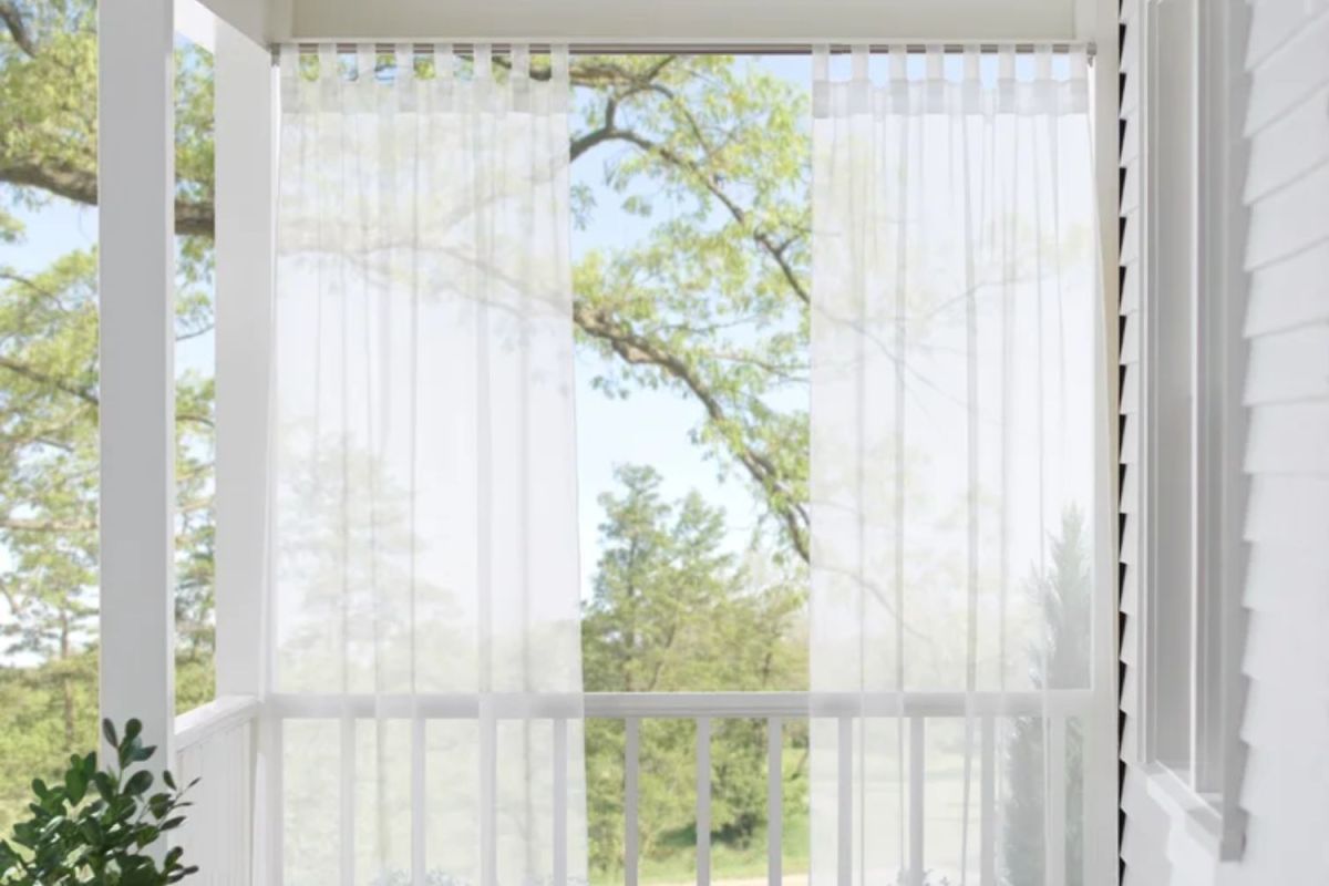 Gauzy white outdoor curtains installed over a window to provide shade, style, and privacy.