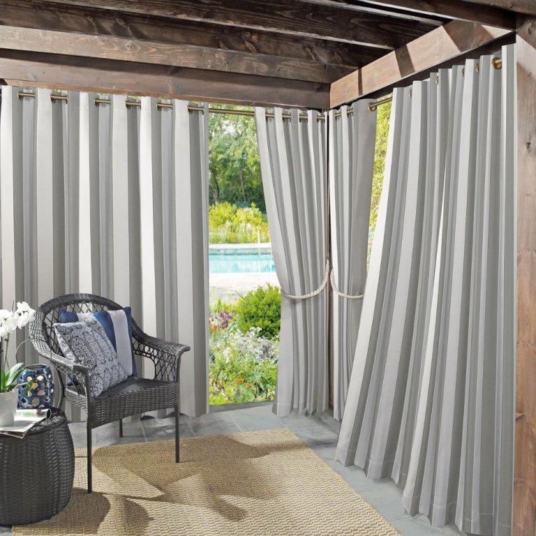  The Sun Zero Valencia Cabana Stripe Outdoor Curtain installed on the corner of a covered deck to provide shade and privacy for a seating area.
