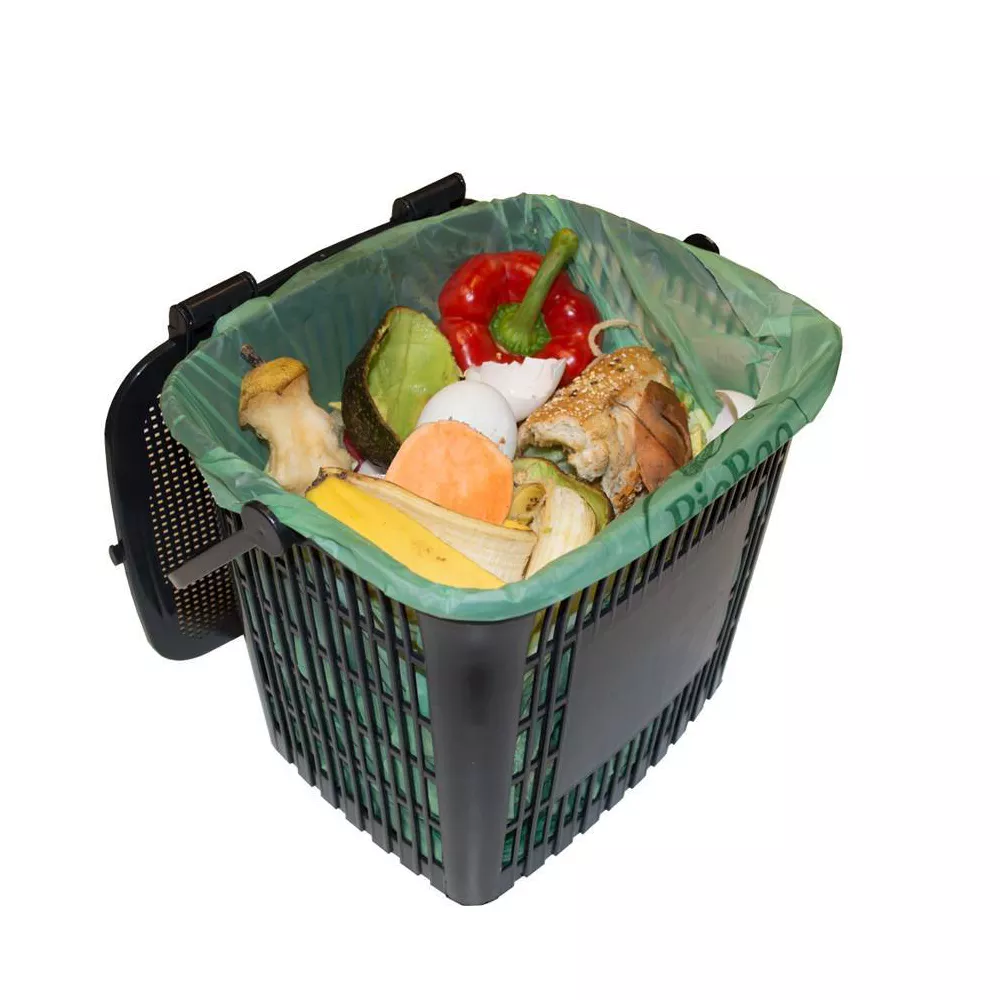 A compost bin with food scraps is lined with a green compostable bag.