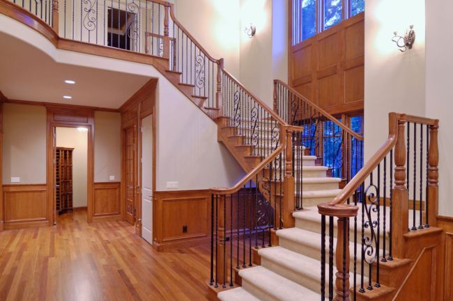 A elegant railing lines white carpeted stairs in an empty home with white walls and hardwood flooring. 